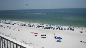 A beach with rows of sunbeds and umbrellas, a clear sky, and a boat in the water.