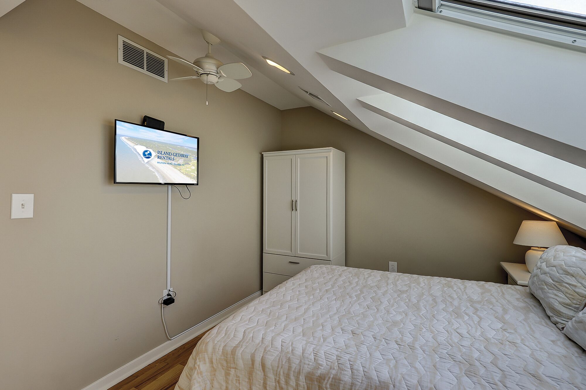 A bedroom with a bed, a wardrobe, a ceiling fan, and a TV displaying 'Island Getaway Rentals'.