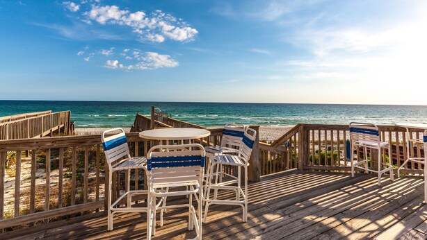 A wooden deck with white chairs and a table overlooking the ocean. - Exclusive private home in gated community across the street from the beach. (PANAMA CITY BEACH)