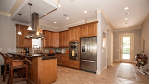 A spacious kitchen with wooden cabinets, stainless steel appliances, and a central island. - Exclusive private home in gated community across the street from the beach. (PANAMA CITY BEACH)