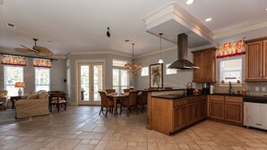 A spacious kitchen with wooden cabinets, a central island, and a dining area with chairs and a table. - Exclusive private home in gated community across the street from the beach. (PANAMA CITY BEACH)