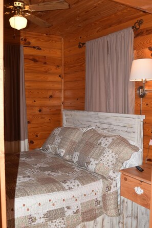 Een houten kamer met een bed, gordijnen, een lamp en een plafondventilator.