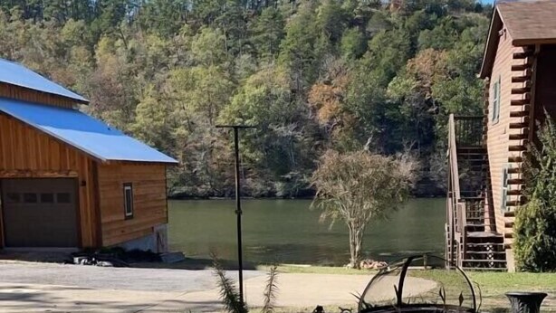 A rustic cabin with a metal roof, a wooden deck, and a view of a lake surrounded by trees.