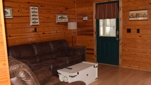 A wooden cabin interior with a brown leather couch, a white storage box, and a green door.