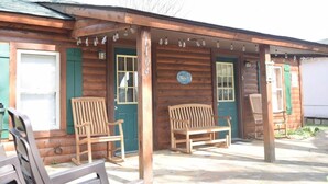 A wooden cabin with a porch, two wooden benches, and a green door.