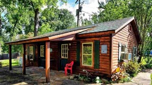 A wooden cabin with a porch, stone patio, and a red chair.