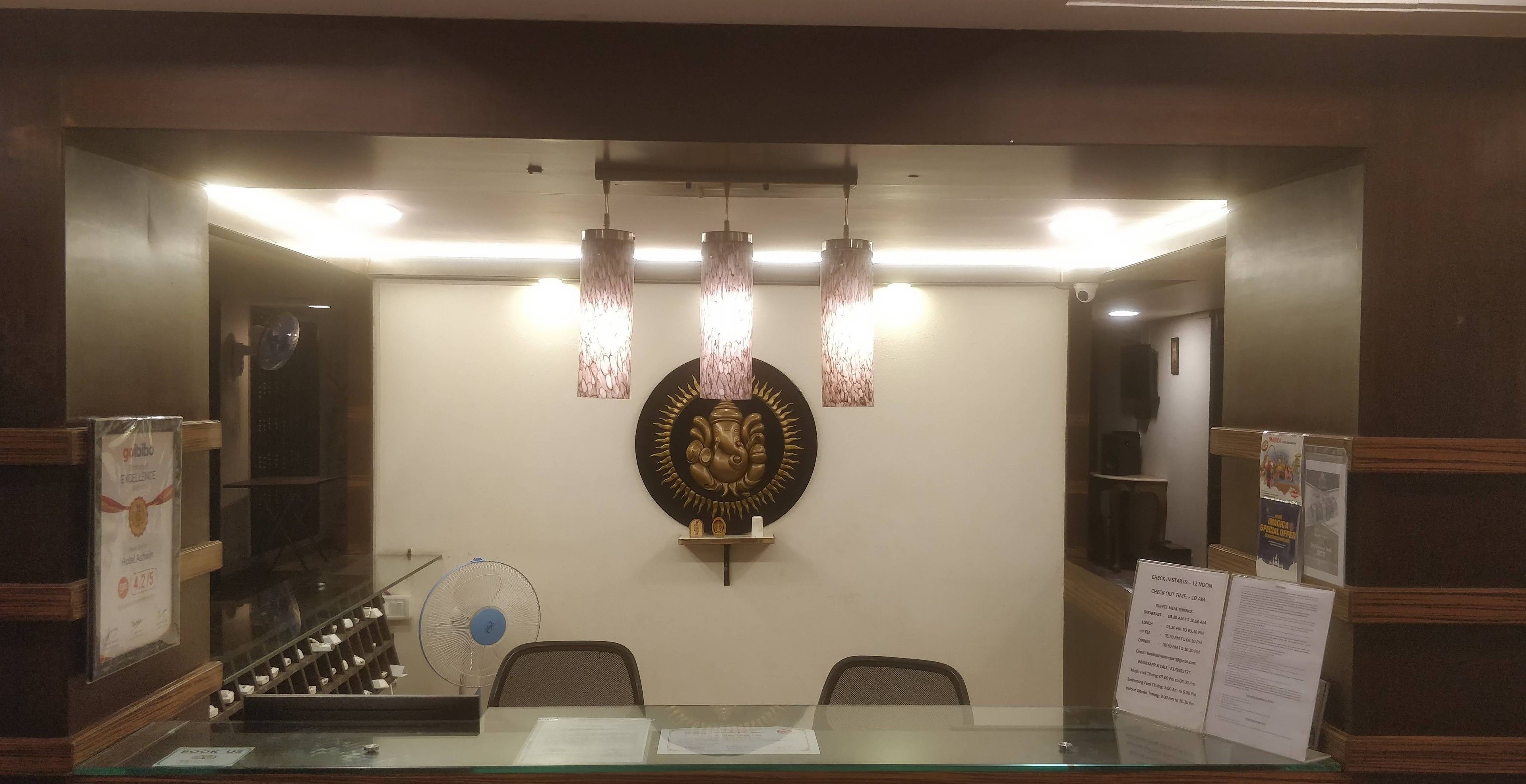 Un área de recepción con mostrador de vidrio, un ventilador, un adorno en la pared y un letrero con los horarios de entrada y salida.
