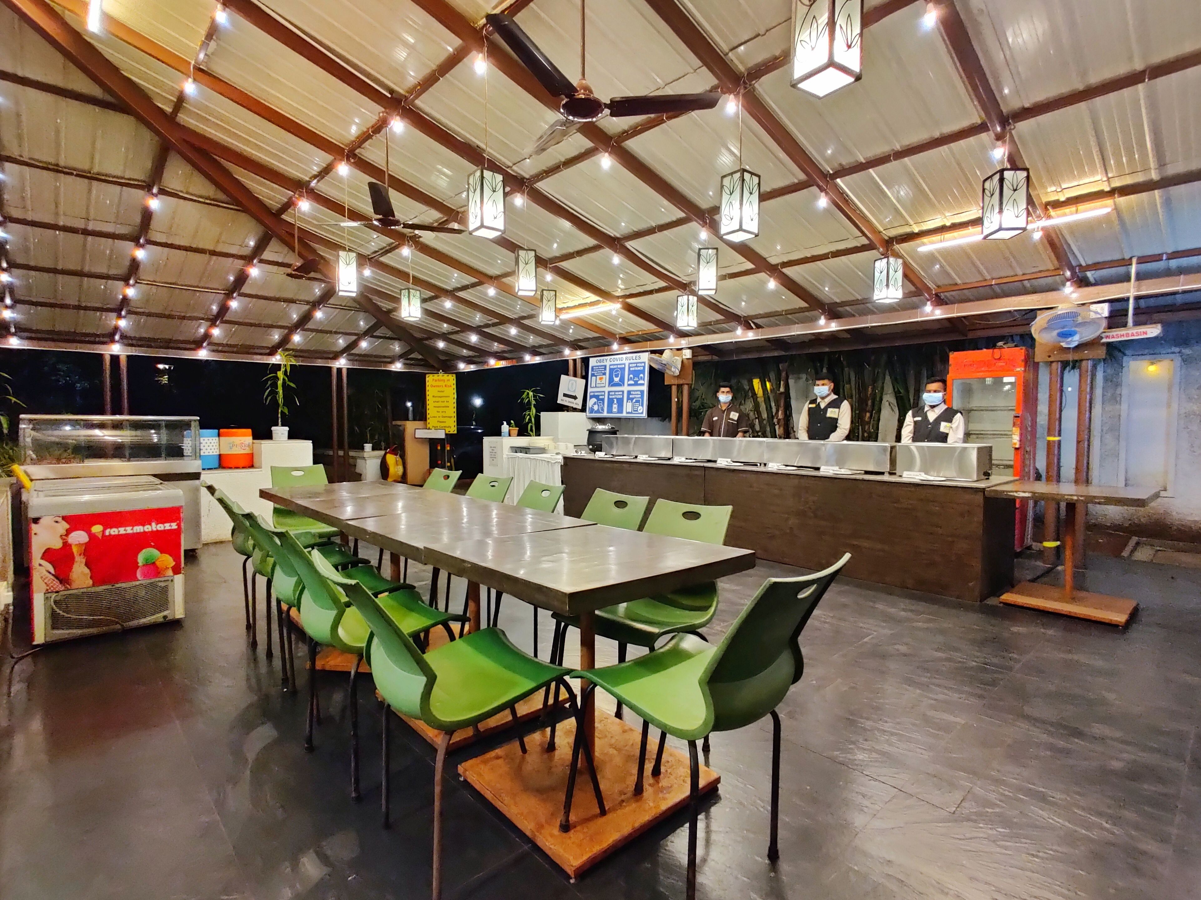 A spacious restaurant with a long counter, green chairs, and a ceiling with hanging lights.