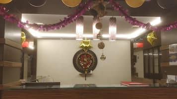 Uma área de recepção com balcão de vidro, um painel decorativo e enfeites pendurados.