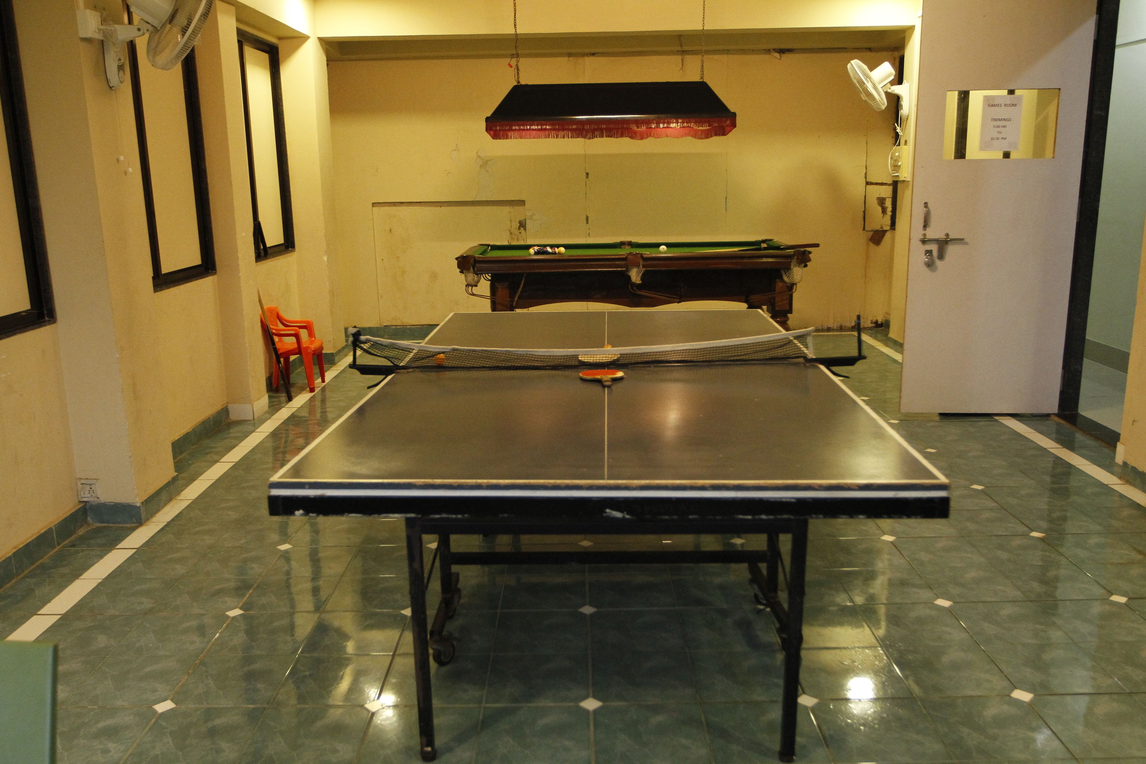 Une table de billard dans une pièce équipée d’une porte, d’une chaise et d’un ventilateur fixé au mur.