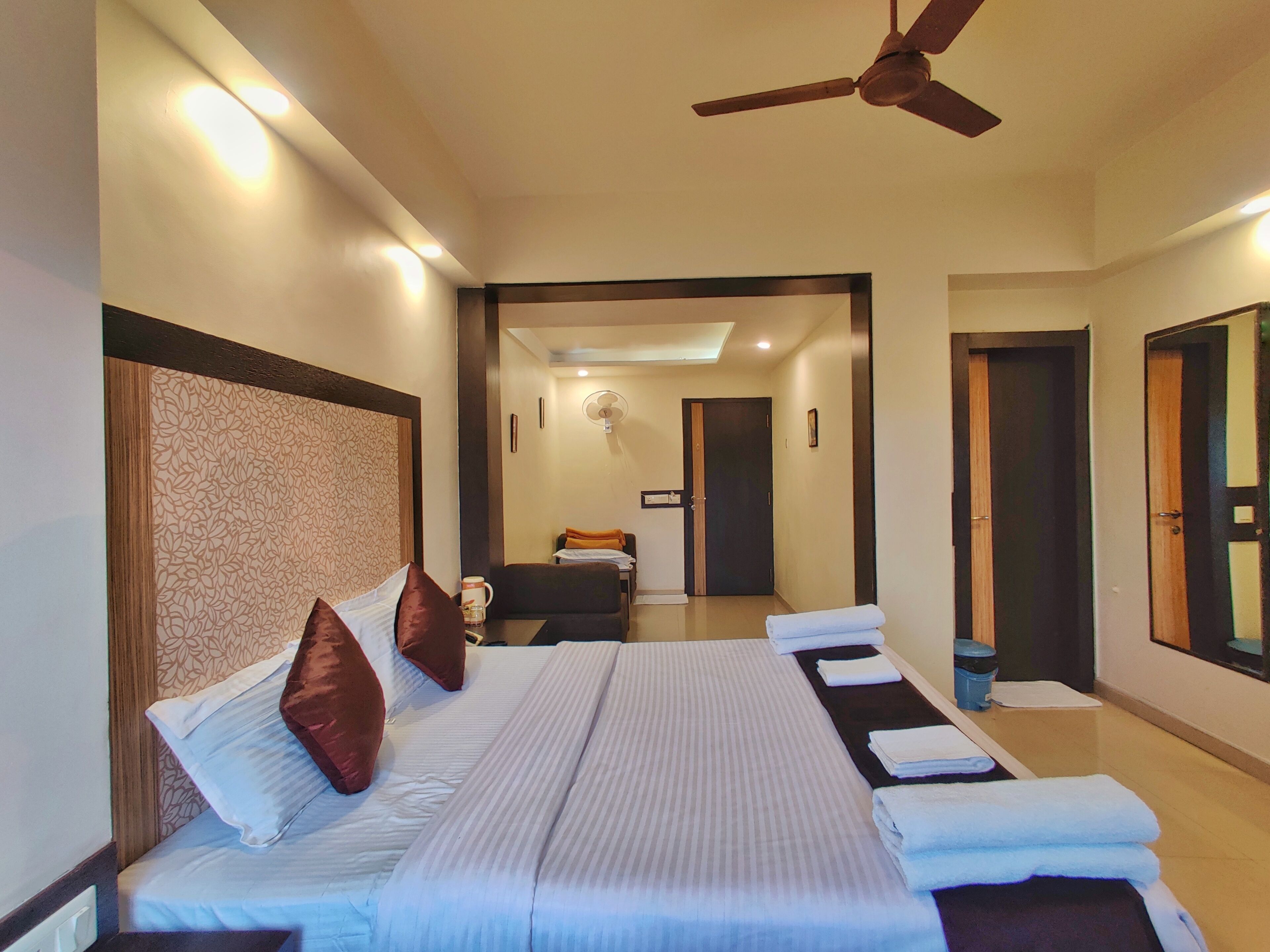 A hotel room with a large bed, a ceiling fan, and a view of the hallway.