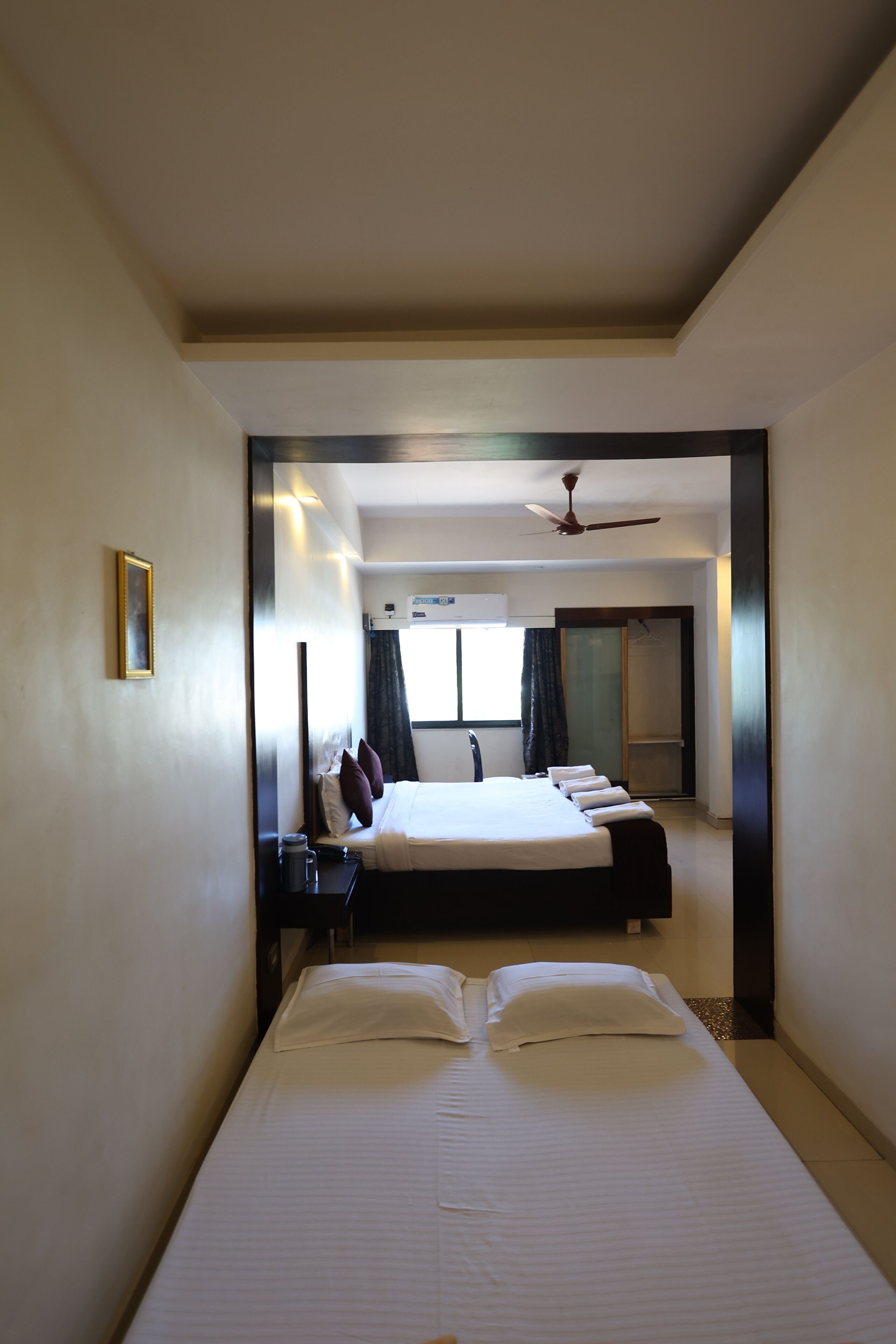 Habitación de hotel con una cama grande, una mesita de noche, un ventilador de techo y una ventana con cortinas.
