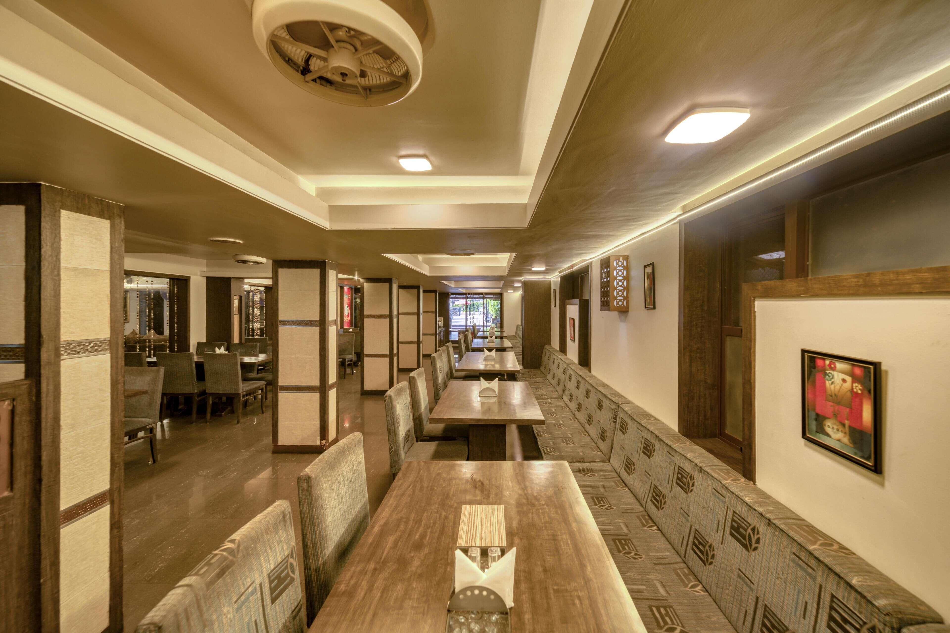 A restaurant with long wooden tables and benches, recessed lighting, and a patterned wall design.