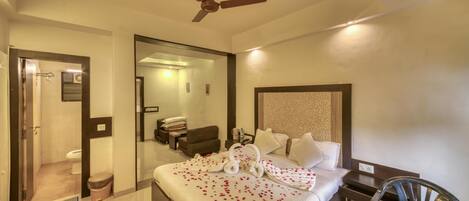 A hotel room with a bed, a ceiling fan, a bathroom, and a nightstand with a lamp.