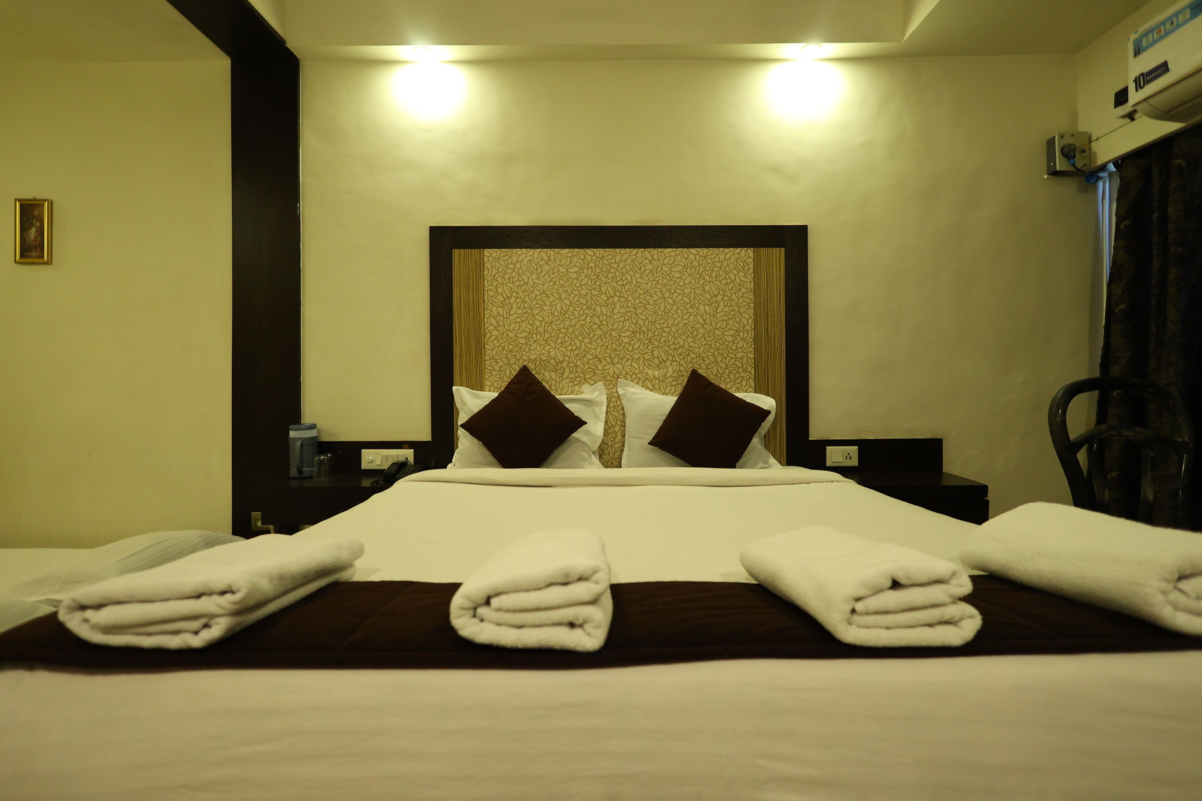 A hotel room with a neatly made bed, a headboard with a patterned design, and a bedside table with a lamp.
