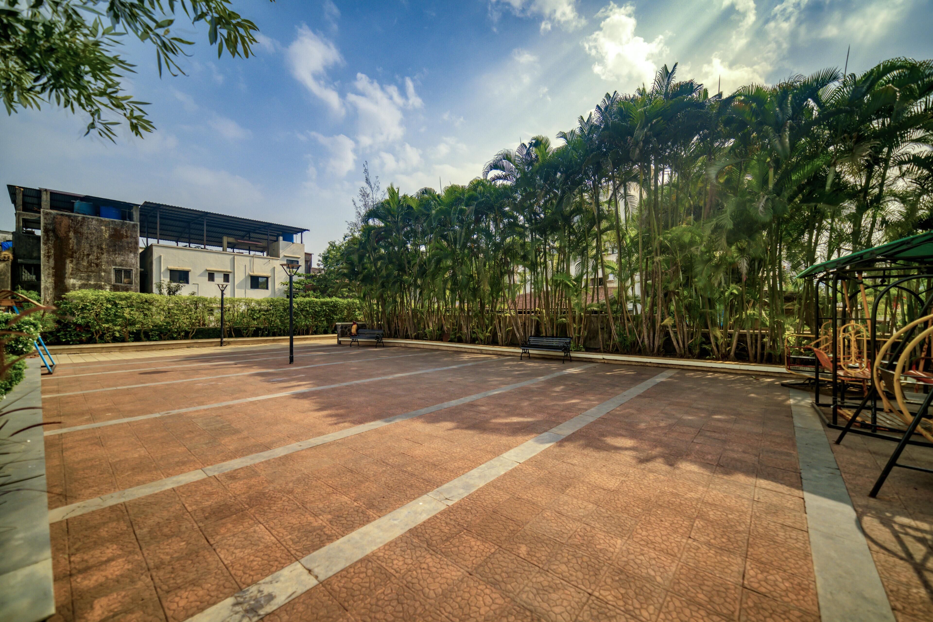 A spacious outdoor area with a paved walkway, benches, and a row of palm trees.