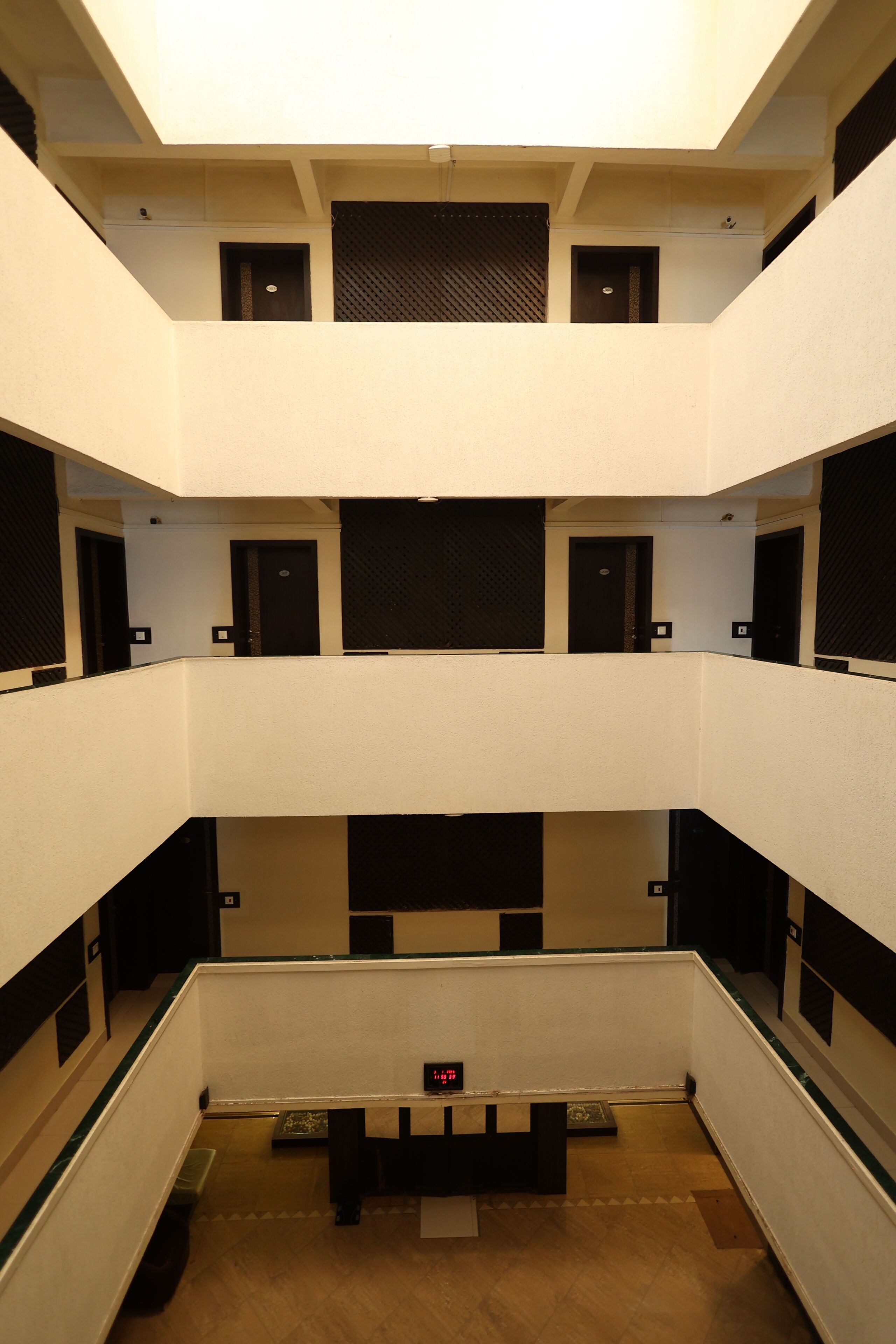 Interior com vários níveis, uma escadaria central, várias portas e um relógio digital.