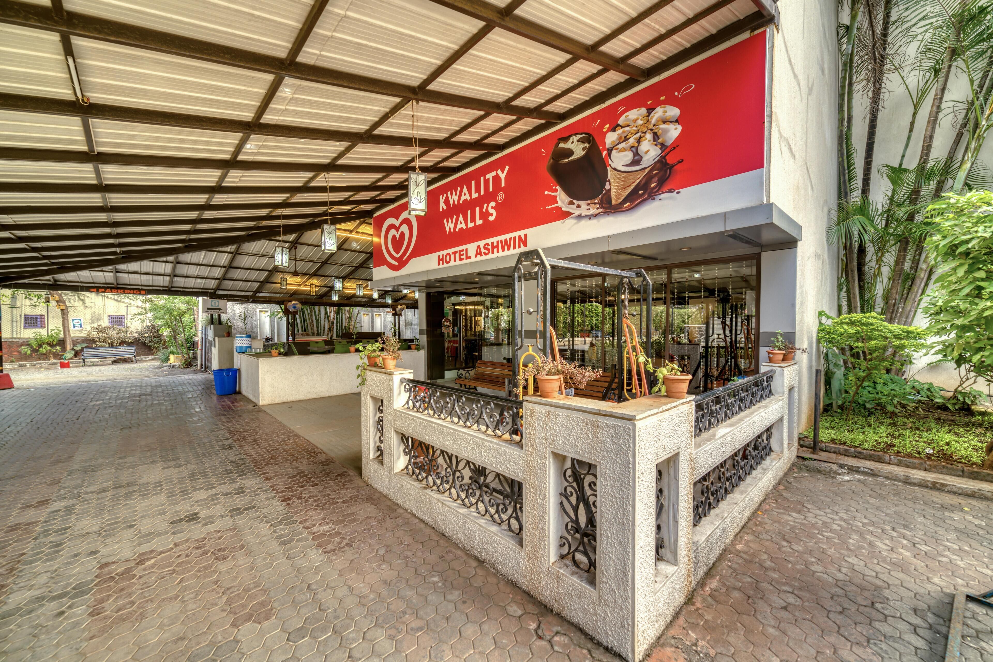 Cafetería llamada "KWALITY WALL'S" con letrero rojo, zona de mesas al aire libre y plantas en macetas.