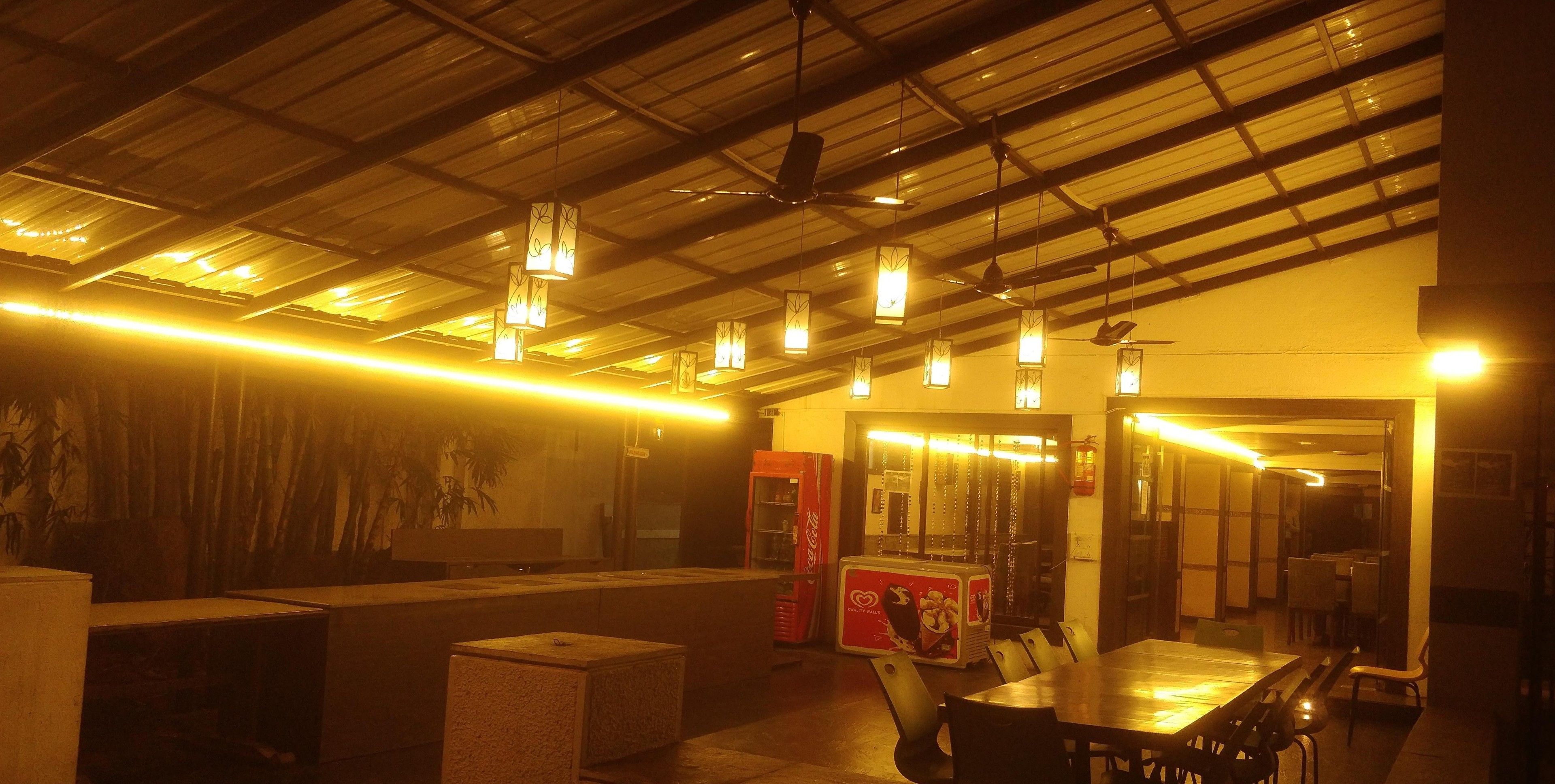 A dimly lit restaurant with hanging pendant lights, a counter, and a seating area with tables and chairs.