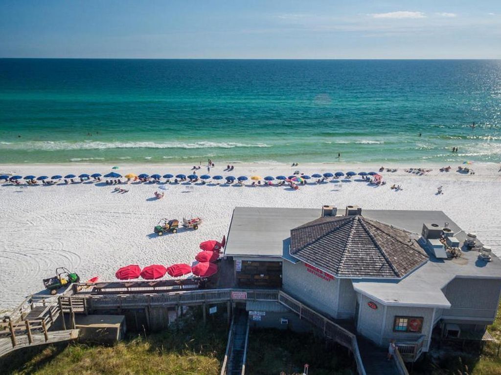 Une plage bordée d’une rangée de parasols et un bâtiment doté d’un toit en pente.