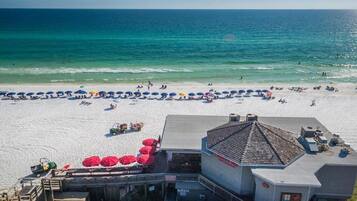 Une plage bordée d’une rangée de parasols et un bâtiment doté d’un toit en pente.