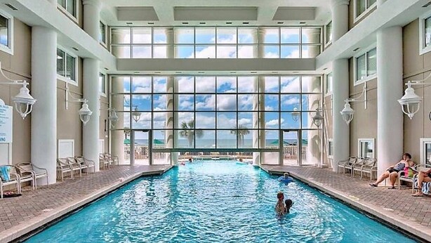 Une piscine intérieure offrant une vue dégagée sur le ciel et les palmiers à l’extérieur.