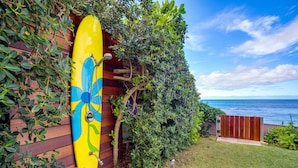 A yellow surfboard leaning against a wooden wall with a view of the ocean. - Beachfront | Sunsets | Spa | Surf Spot (Haleiwa)
