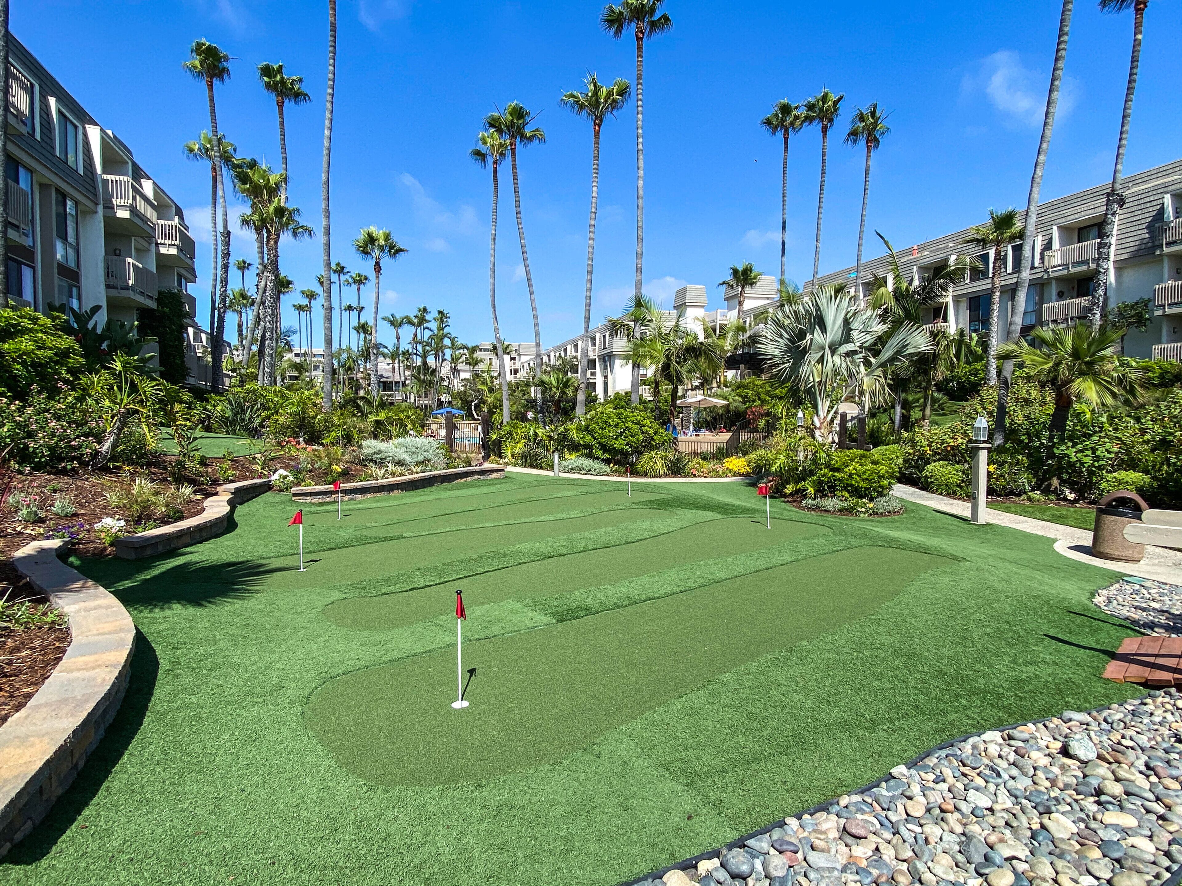 A golf course with a putting green surrounded by palm trees and a pool area.