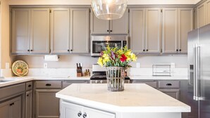 Una cocina moderna con armarios grises claros, un refrigerador de acero inoxidable, una isla central con un florero y una lámpara colgante.