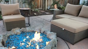 Un patio con dos sofás beige acolchados, una mesita redonda y un brasero con piedras azules.
