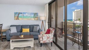 Un balcón con vistas al océano y edificios, un sofá gris con cojines, una mesa de centro de madera y un sillón estampado.