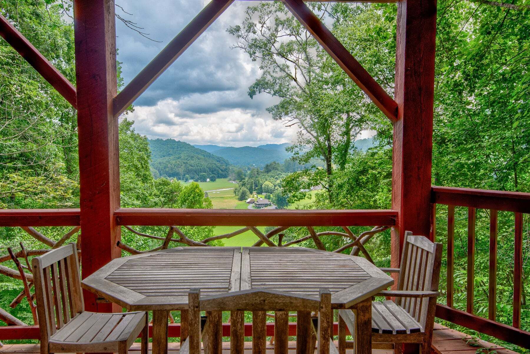 A wooden deck with a table and chairs, overlooking a green landscape with trees and a house.