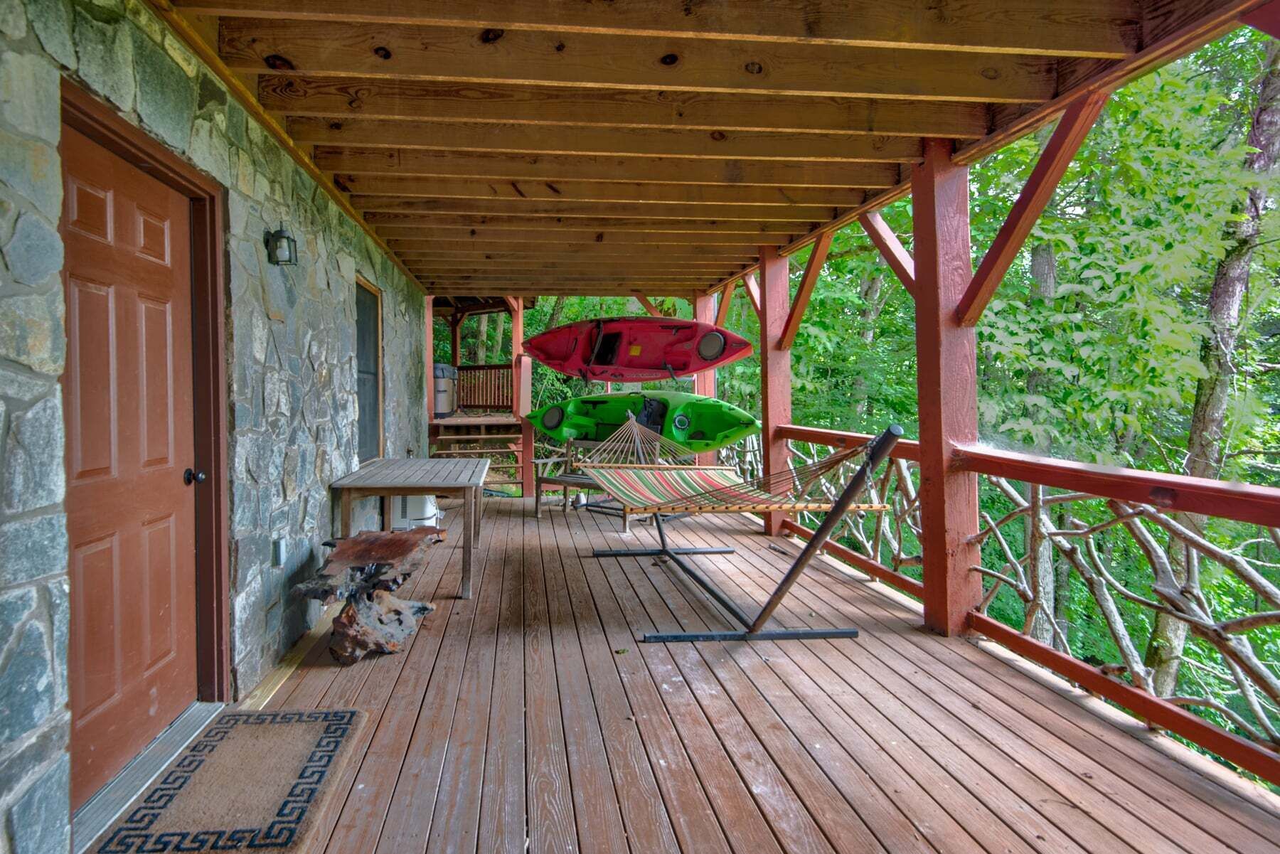 Una terraza de madera con techo, una mesa, sillas y dos kayaks.