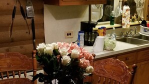 A wooden dining table with a vase of flowers, a wooden chair, and a wooden cabinet in the background. - LOG Cabin, 5 miles from town, but very country setting (Science Hill)
