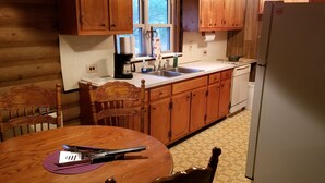 A wooden kitchen with a dining table, chairs, a coffee maker, and a refrigerator. - LOG Cabin, 5 miles from town, but very country setting (Science Hill)
