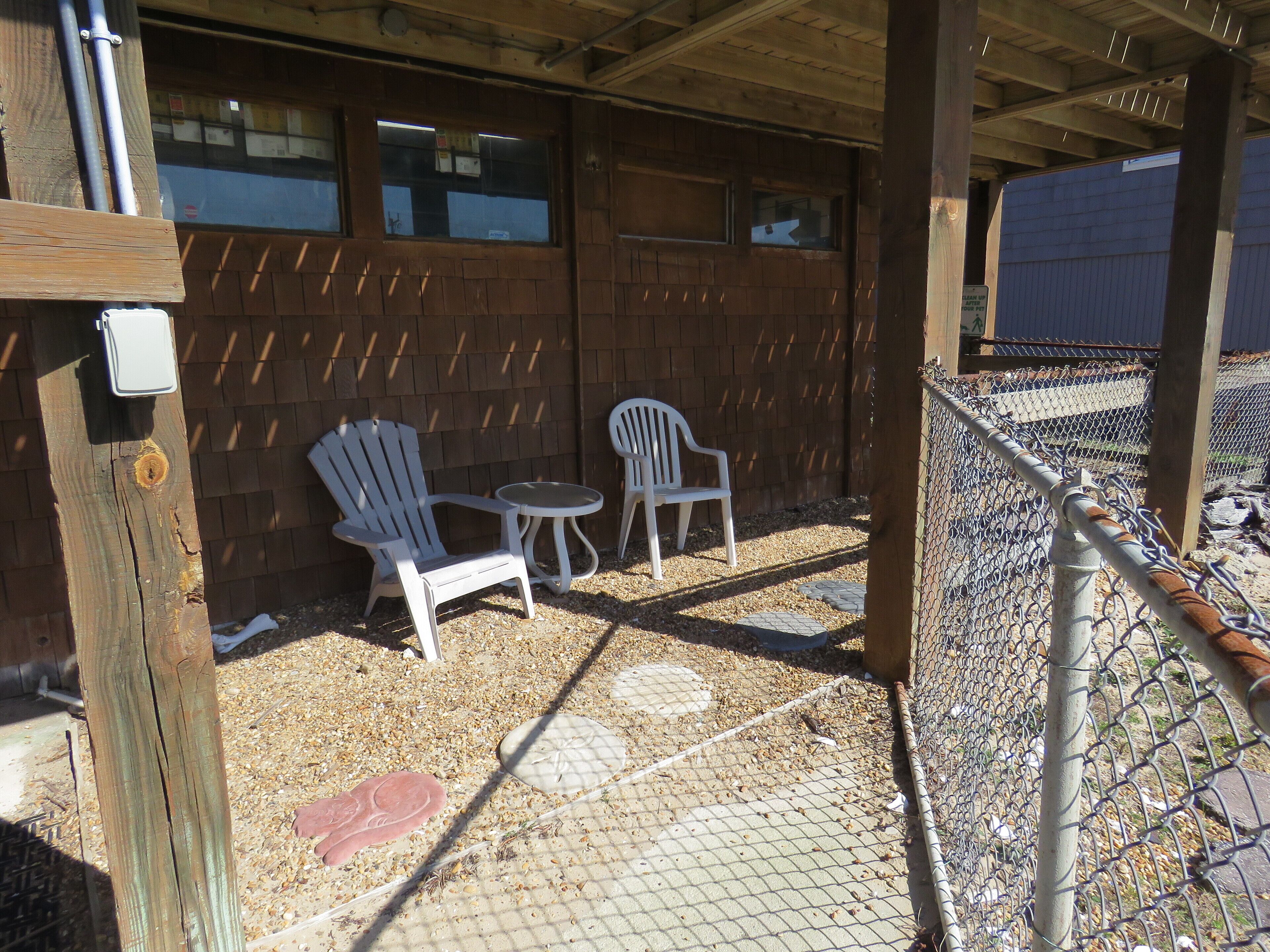 A covered outdoor seating area with two white plastic chairs and a small round table.