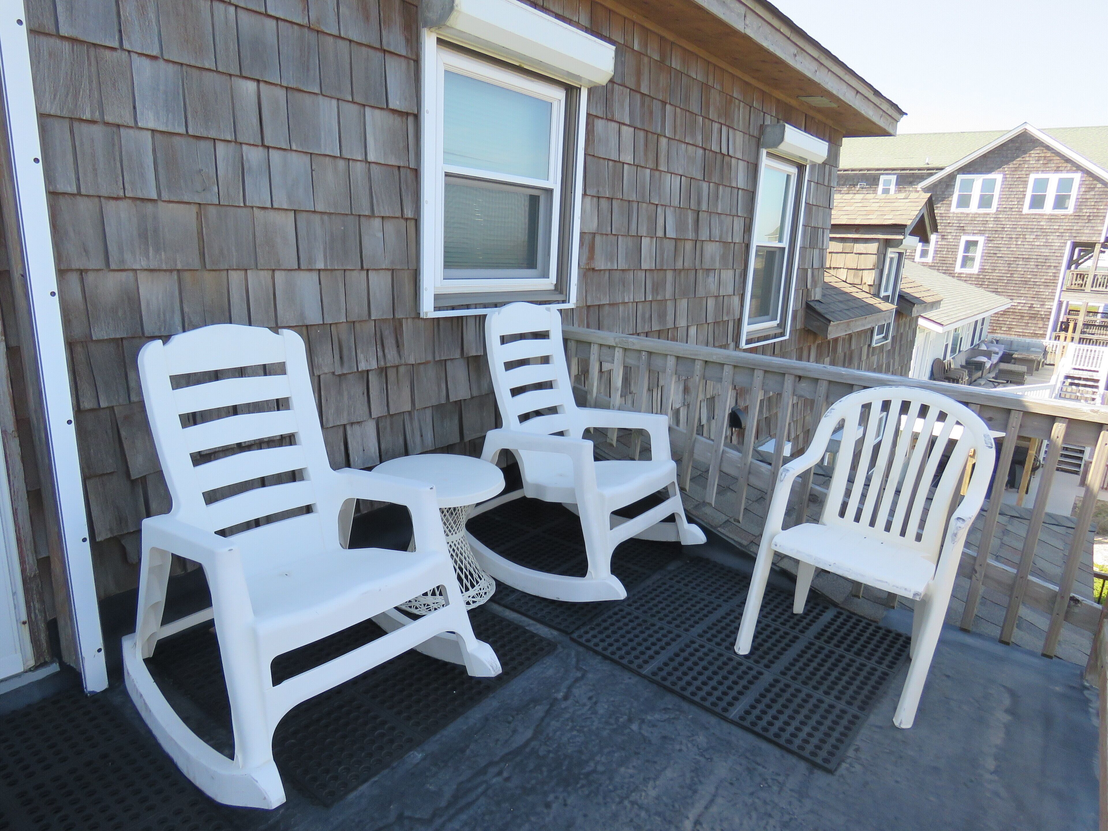 A wooden deck with three white rocking chairs and a small table.