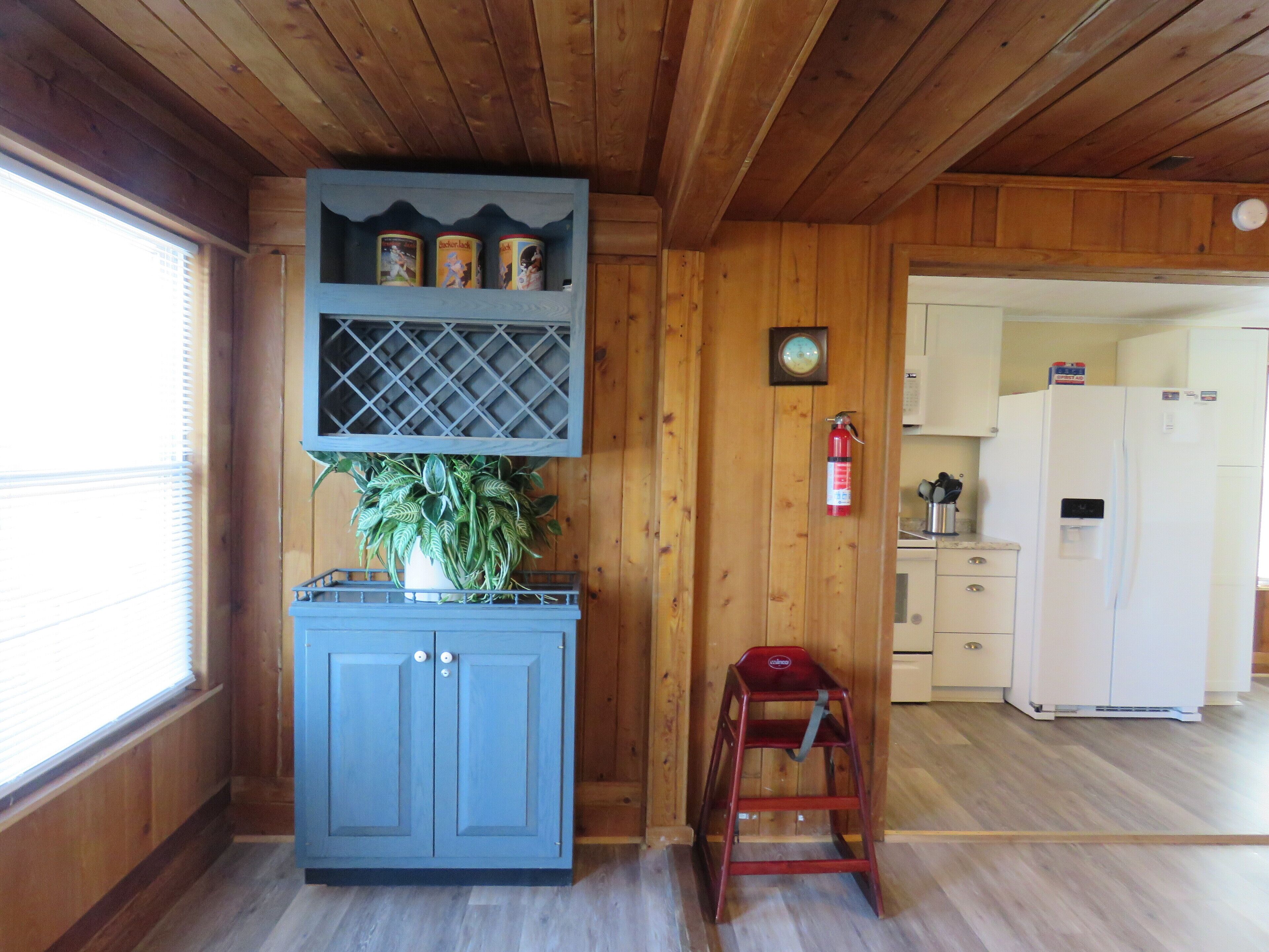 A wooden interior with a blue cabinet, a plant, a fire extinguisher, and a kitchen area.