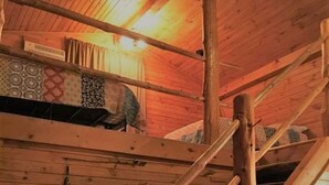 Un interior rústico de madera con techo inclinado, vigas a la vista y una cama sencilla.
