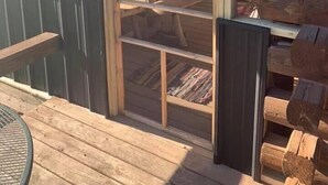 Una terraza de madera con un ventanal de vidrio que da a un espacio exterior con una mesa de picnic y bancos.
