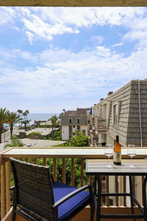 A balcony with a view of the ocean, a table with a bottle and glasses, and a chair.