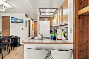 Una cocina con armarios de madera, un refrigerador blanco y una zona de bar con dos sillas.