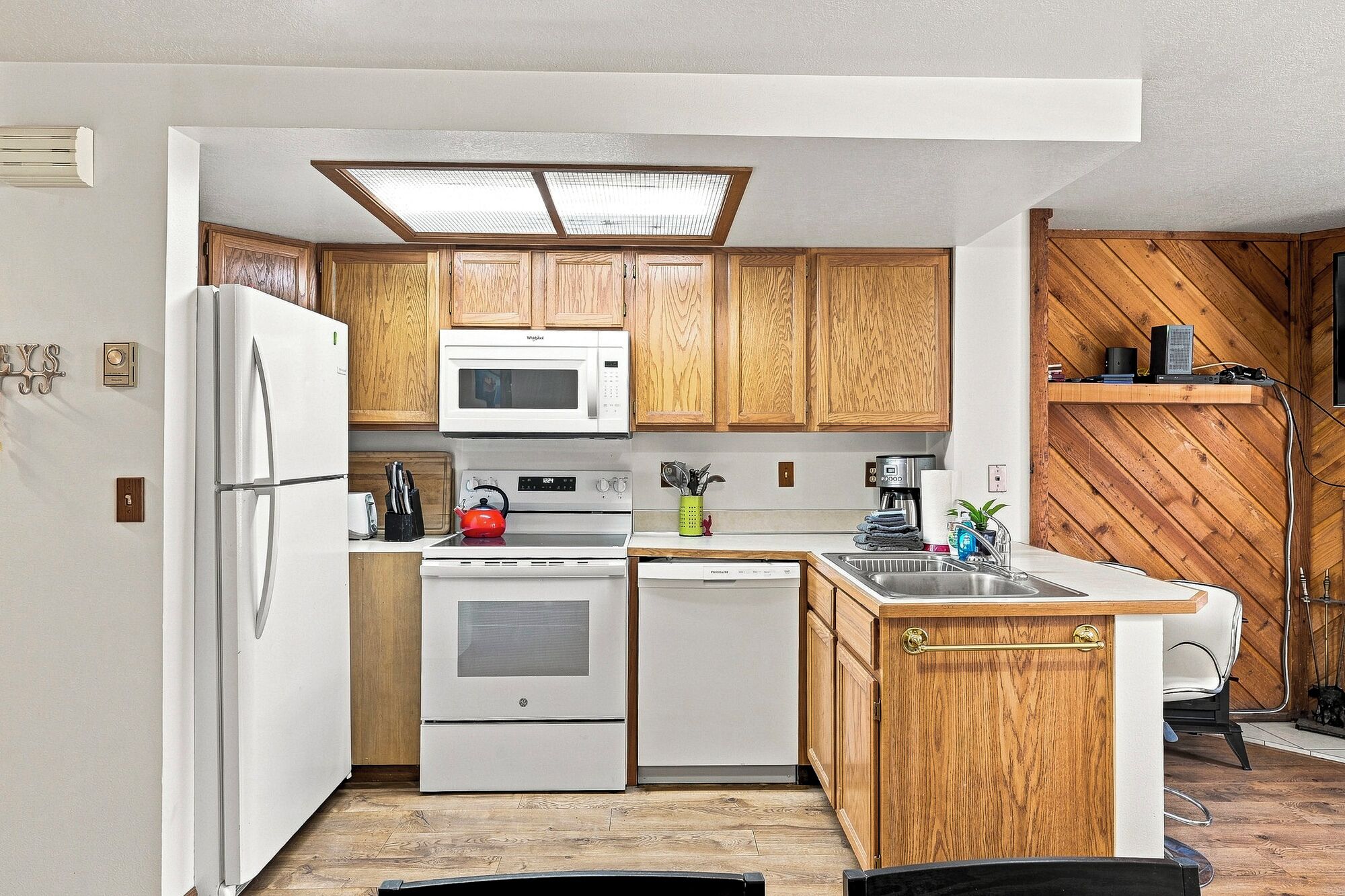 Una cocina compacta con armarios de madera, microondas, estufa, lavavajillas y pileta.