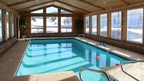 Una piscina interior con ventanales amplios, paredes de madera y vistas a un paisaje nevado.