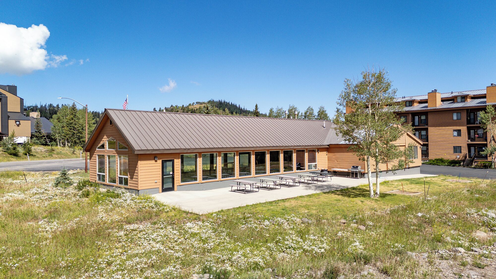 Un bâtiment moderne doté d’un toit en pente, de grandes fenêtres et d’un espace extérieur aménagé pour s’asseoir.