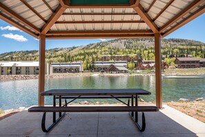 Un área de picnic techada con vista a un lago y edificios al fondo.