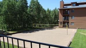 A volleyball court with a yellow net, surrounded by a fence, trees, and a building with balconies. - Brian Head Timberbrook Studio close to ski slopes sleeps 4 (Brian Head)