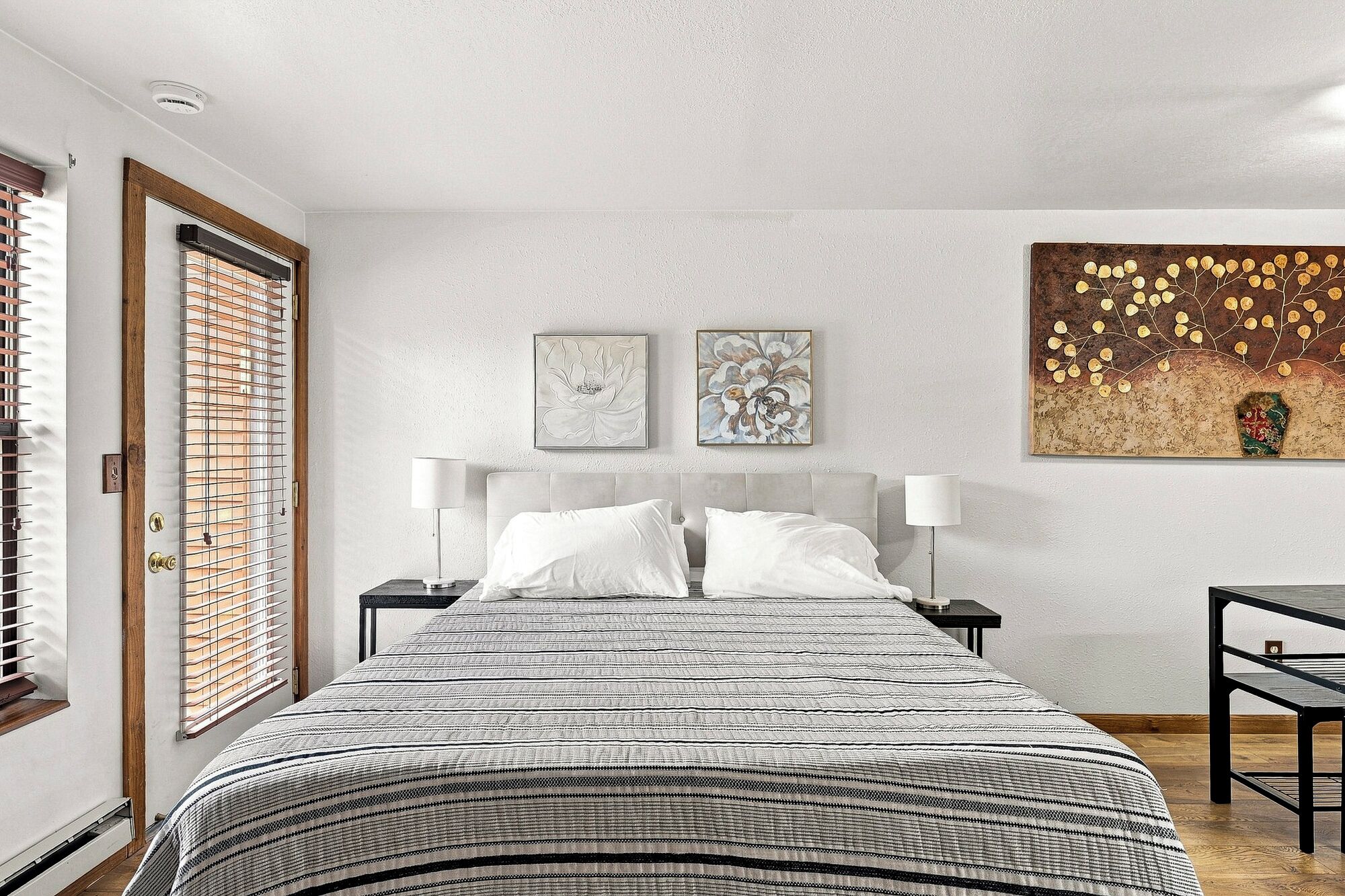 Un dormitorio con cama, dos mesitas de noche, un escritorio y una obra de arte en la pared.
