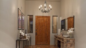 Un pasillo con puerta de madera, candelabro, consola decorada y alfombra estampada.