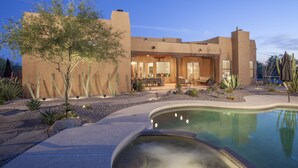 Una casa moderna con piscina, mobiliario exterior y jardines con vegetación desértica.